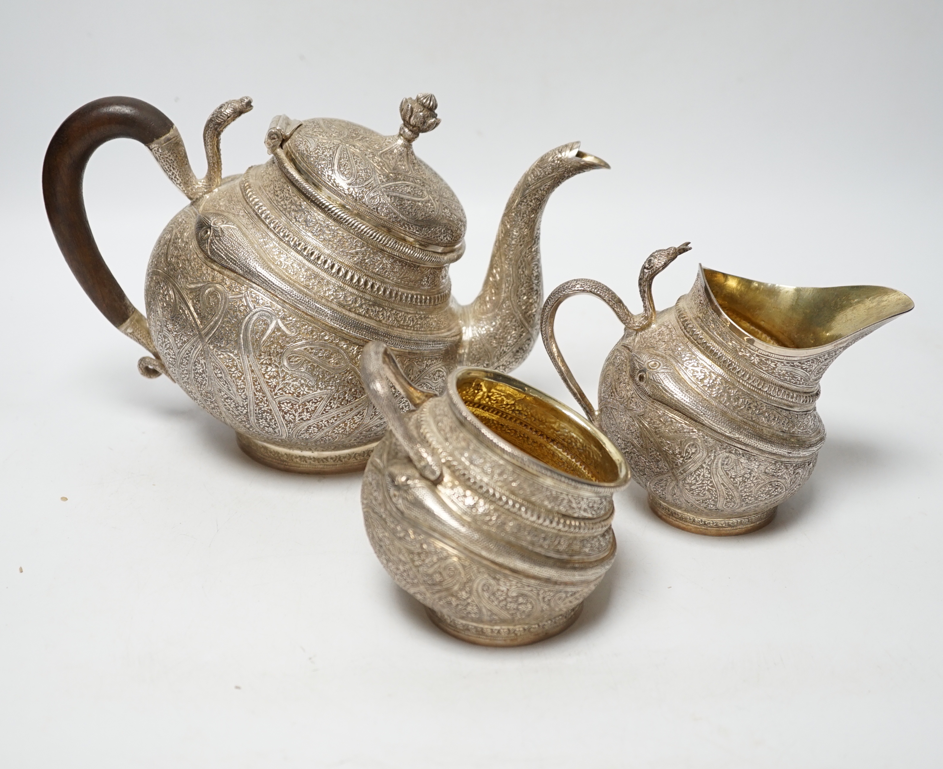 A 20th century Indian three piece embossed white metal tea set, with boteh and cobra decoration, gross weight 38.6oz.